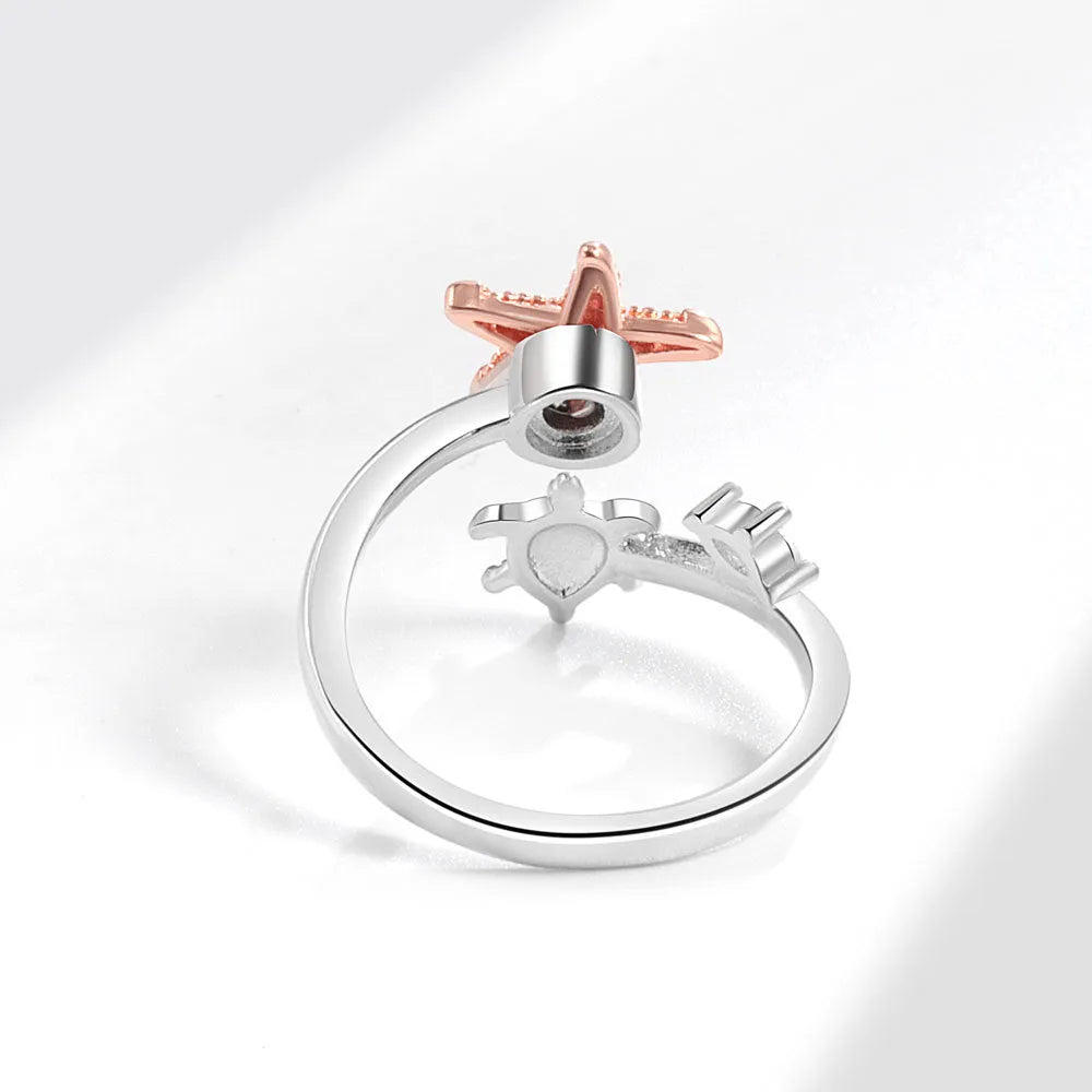 White gold copper spinning anxiety relief ring with turtle and starfish elements on a flat surface