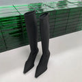 Black pointed toe below the knee women's boots with a stiletto heel and back zipper closure on a white background.