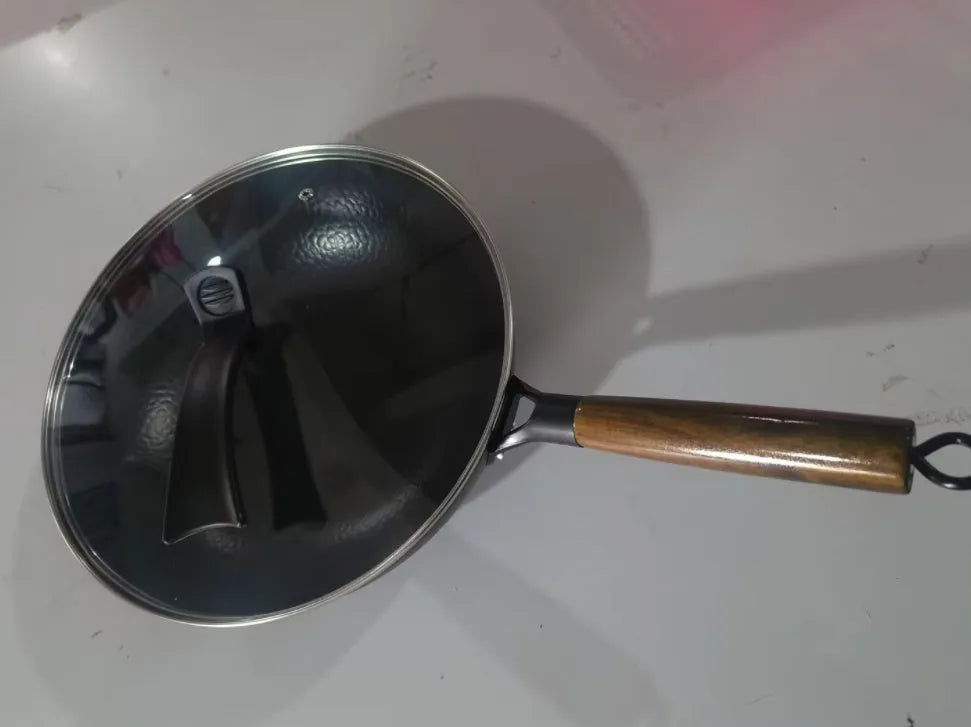 Black traditional handmade iron wok pan with a long wooden handle on a kitchen hob.