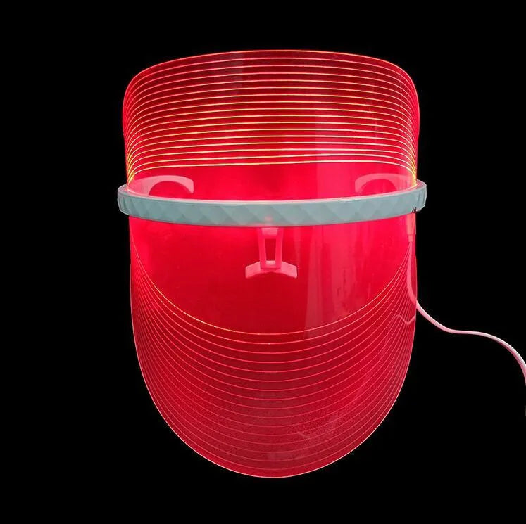 Transparent ABS LED light therapy face mask with red blue yellow lights and USB cable on a flat surface