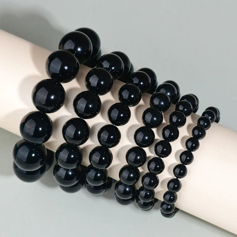 Hand-woven round obsidian bracelet with crystal beads in various colour options on a wrist.