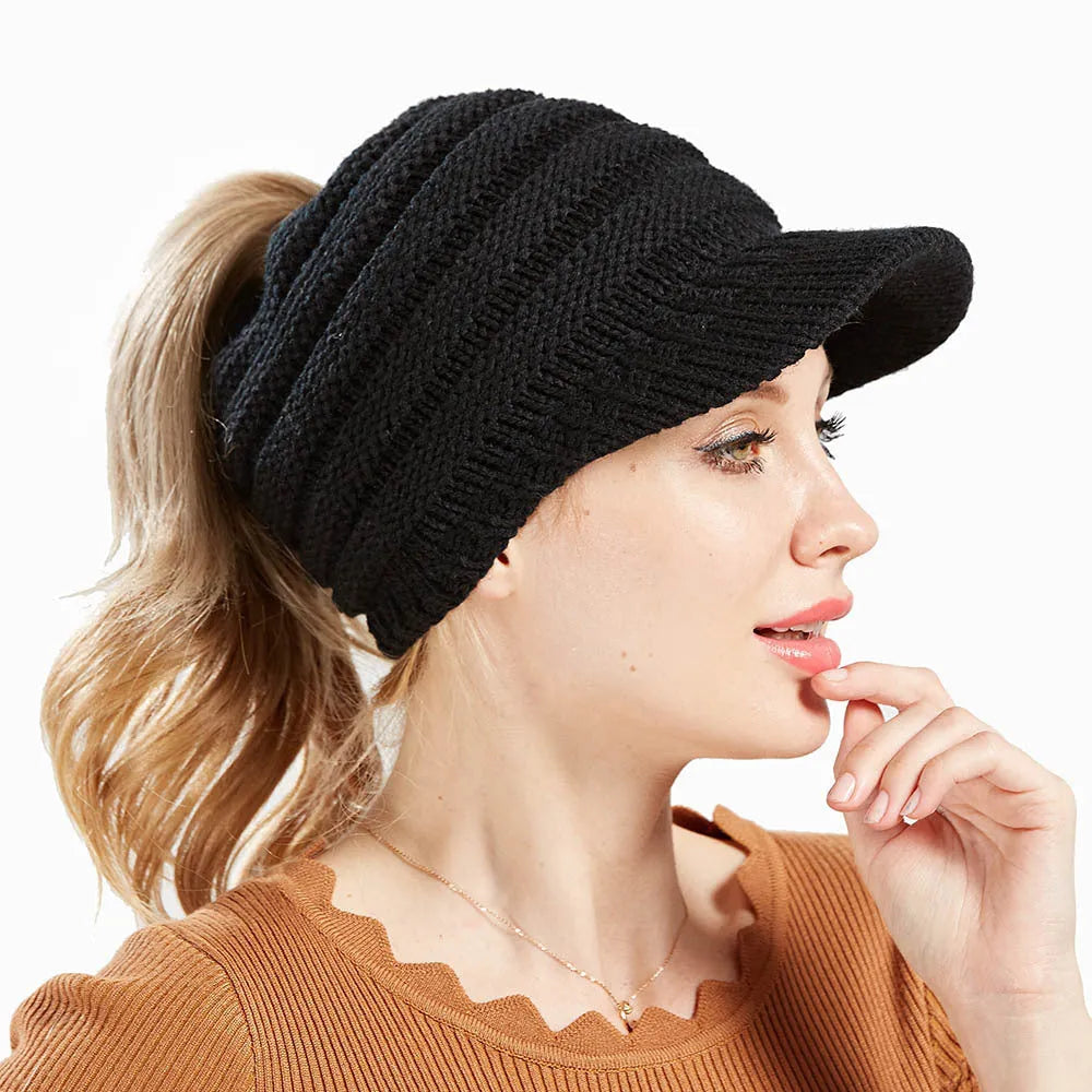Woman wearing a light grey knitted beanie with a ponytail pulled through the back opening.