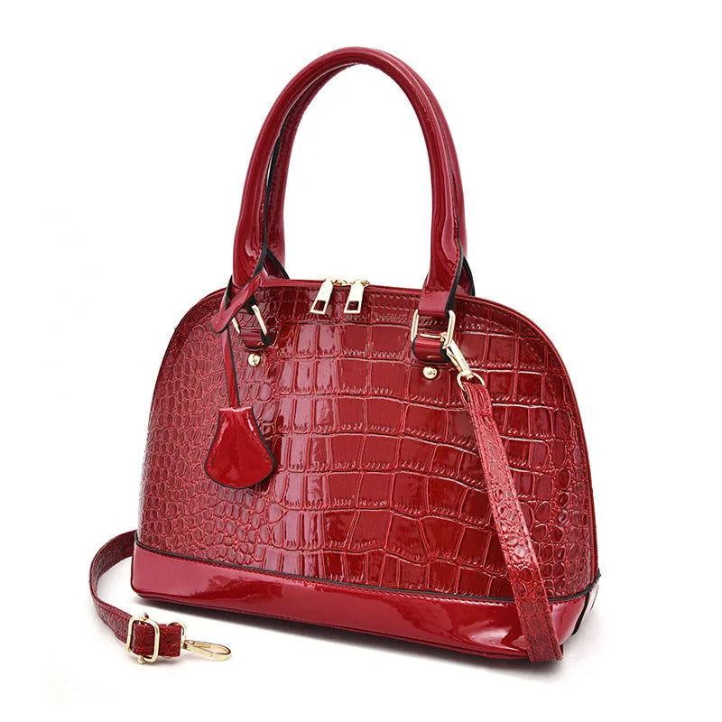 Large shiny black crossbody shoulder bag showing structured shell shape and dimensions