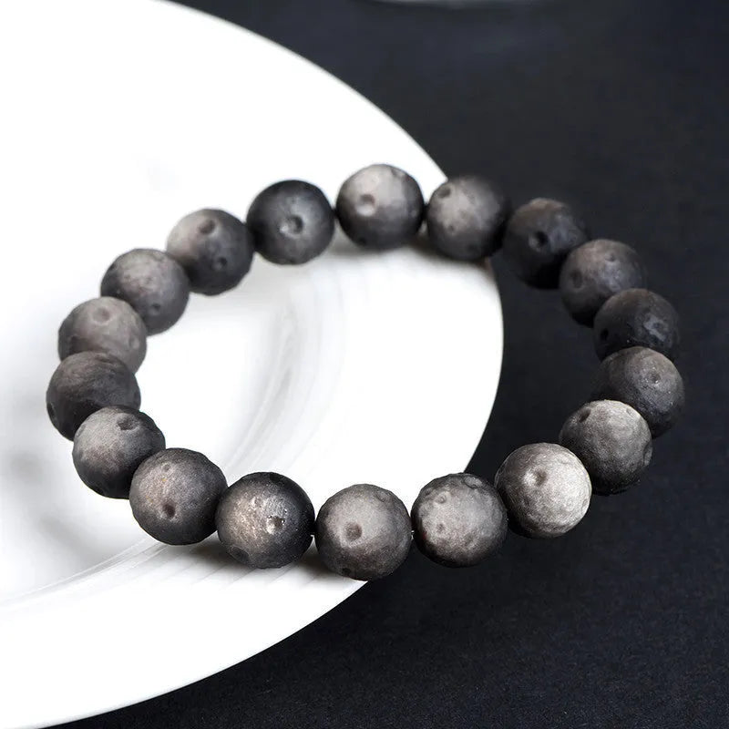 Natural obsidian crater ball bracelet showing polished spherical beads in silver stone meteorite colour with visible mineral texture