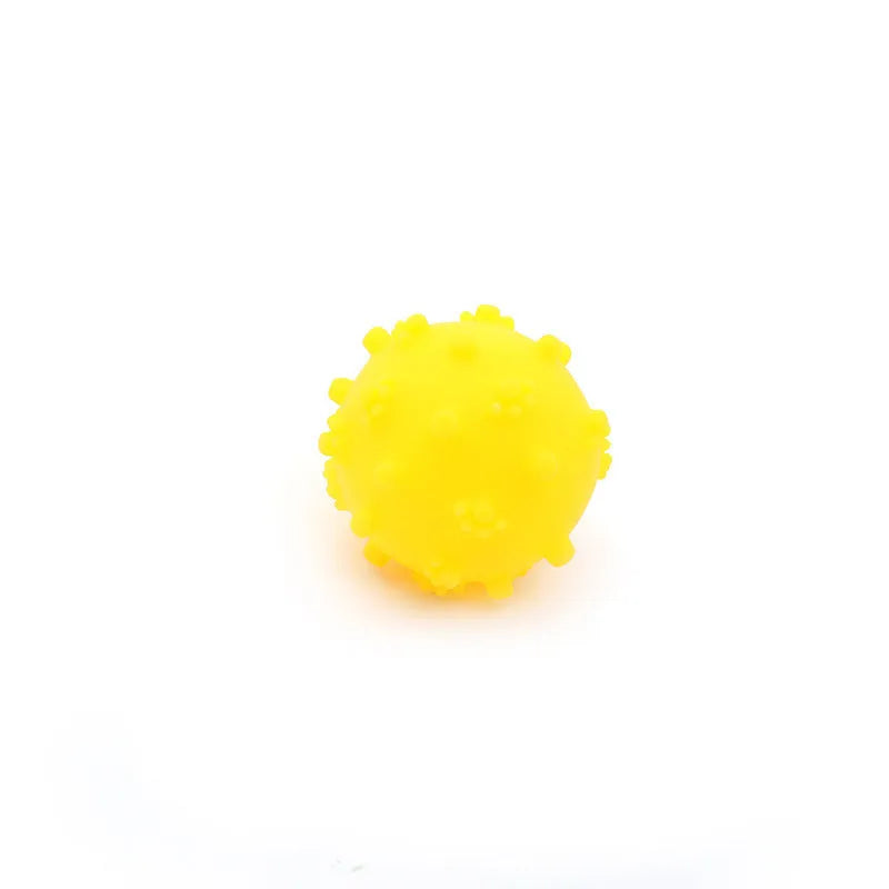 Blue, green, pink, and yellow 2-inch dog balls with spiked dimple texture on grass.