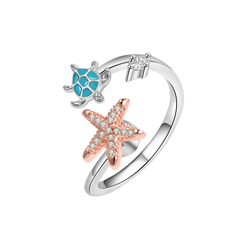 White gold copper spinning anxiety relief ring with turtle and starfish elements on a flat surface