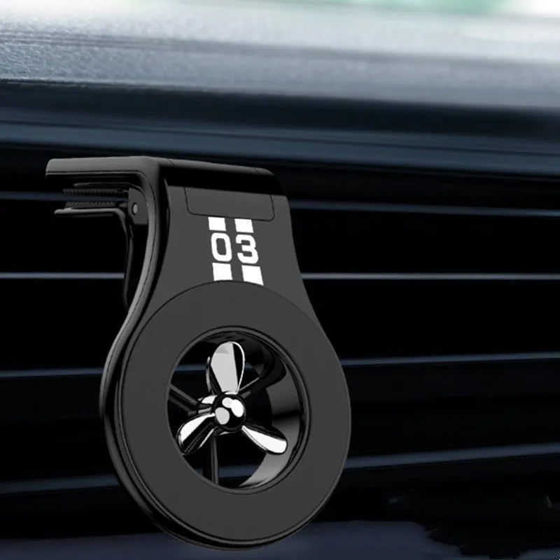 Black magnetic car phone holder clipped to a car air vent, holding a mobile phone, with a fragrant slice inserted.