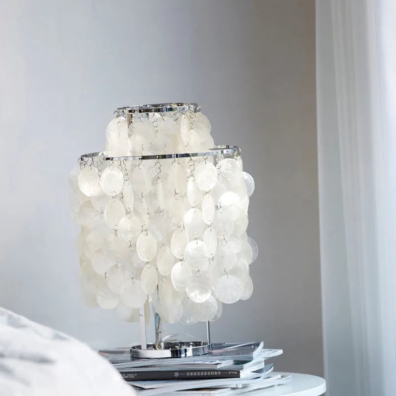 Modern shell-shaped bedside table lamp in chrome metal finish on a wooden surface.