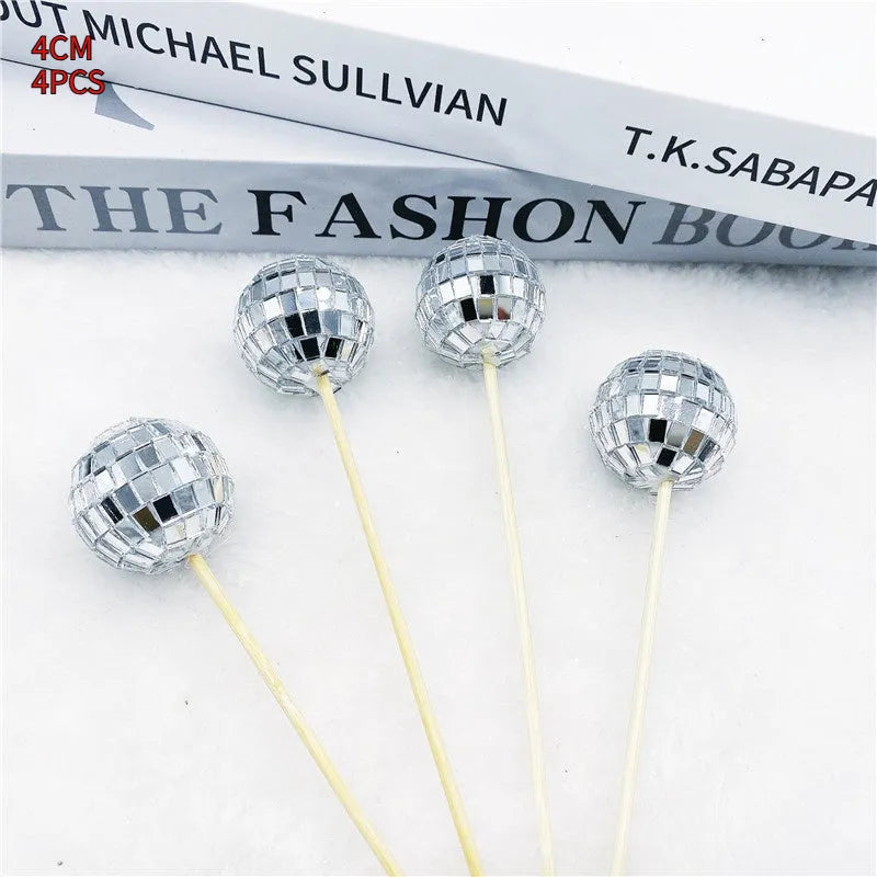 Glass disco ball cake decoration with a wooden stick inserted into a cake, showing reflective surface.