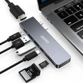 Silver 7-in-1 USB-C hub adapter with SD card reader, HDMI, and USB ports on a wooden desk.