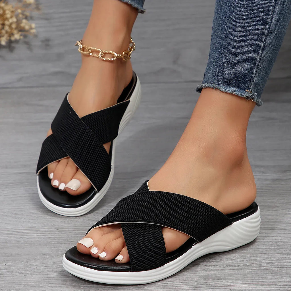 Women's black wedge slippers with a cross strap and peep-toe open front on a thick rubber sole.
