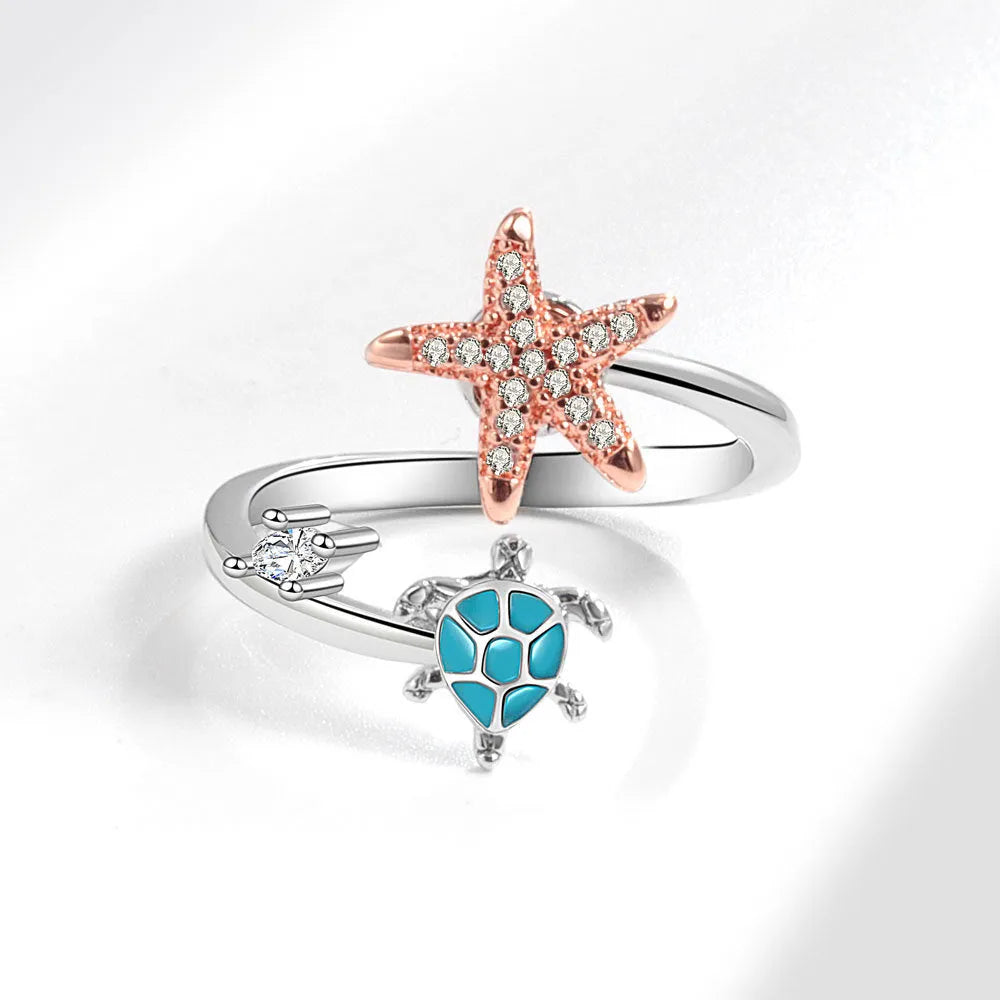 White gold copper spinning anxiety relief ring with turtle and starfish elements on a flat surface