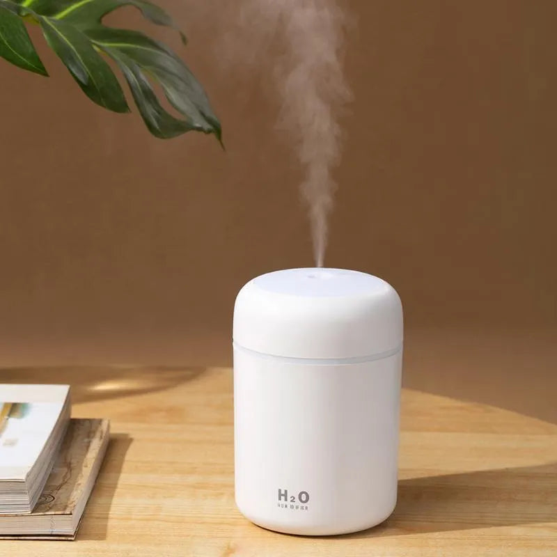 Pink USB desktop humidifier with LED lights next to a white mug on a desk