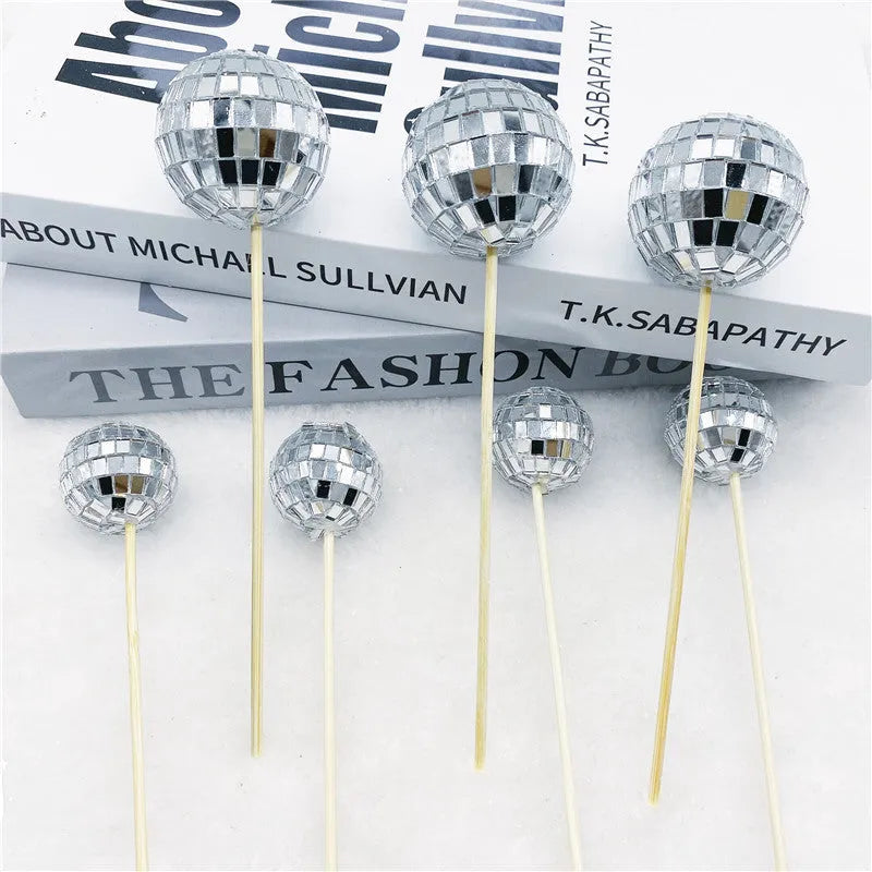 Glass disco ball cake decoration with a wooden stick inserted into a cake, showing reflective surface.