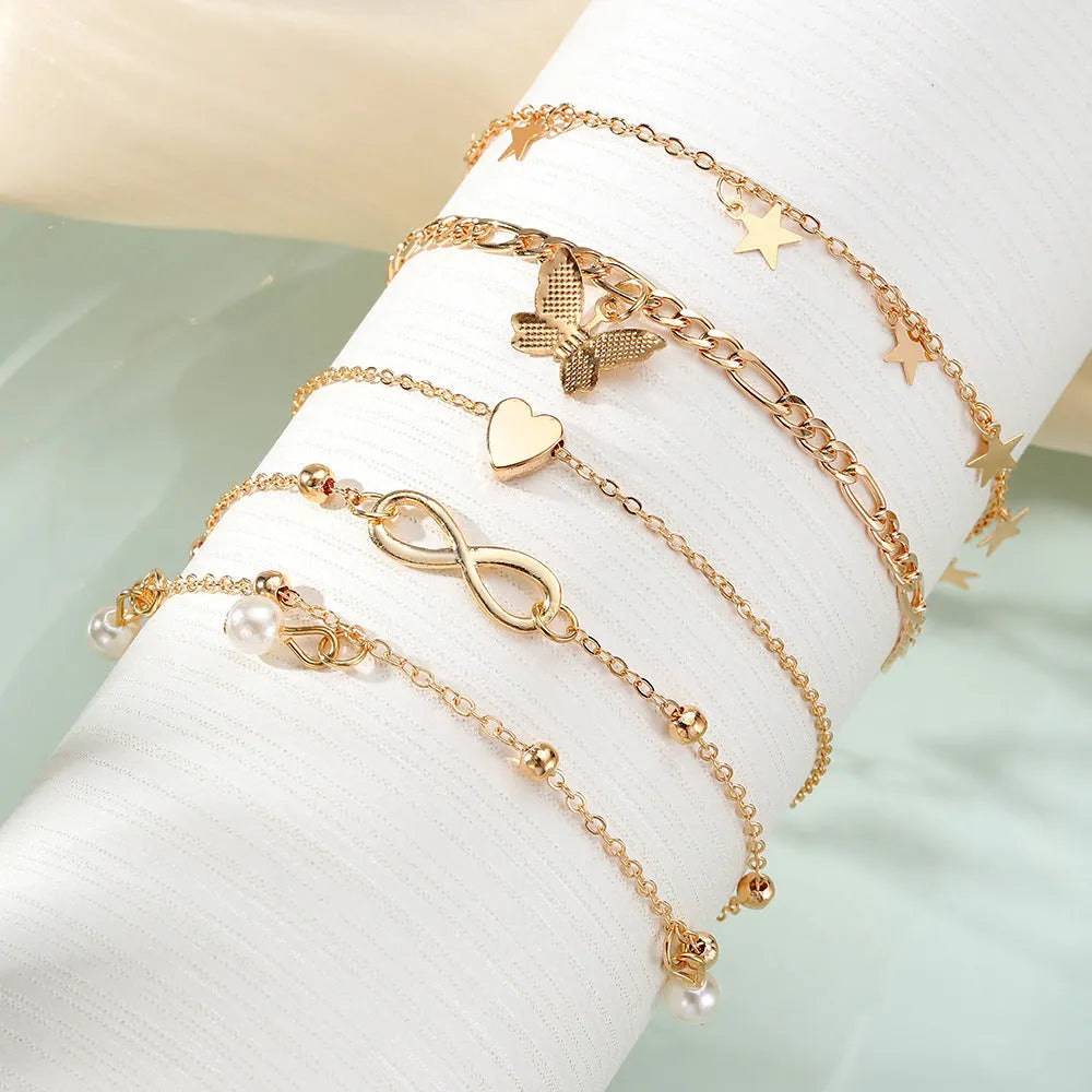 Four alloy anklets with butterfly, pearl and heart charms arranged as a layered jewellery set
