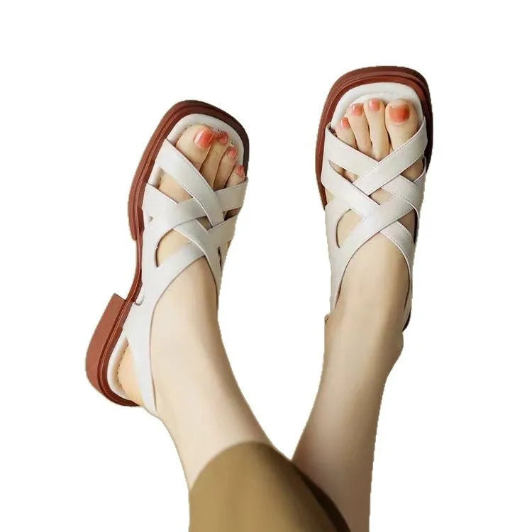 Women's glossy patent leather sandals with cross-belt straps, square toe, and a low block heel.