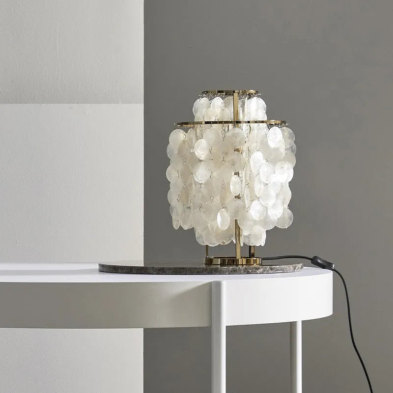 Modern shell-shaped bedside table lamp in chrome metal finish on a wooden surface.