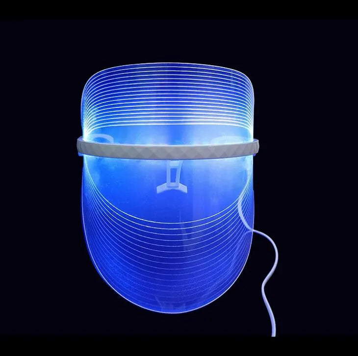 Transparent ABS LED light therapy face mask with red blue yellow lights and USB cable on a flat surface