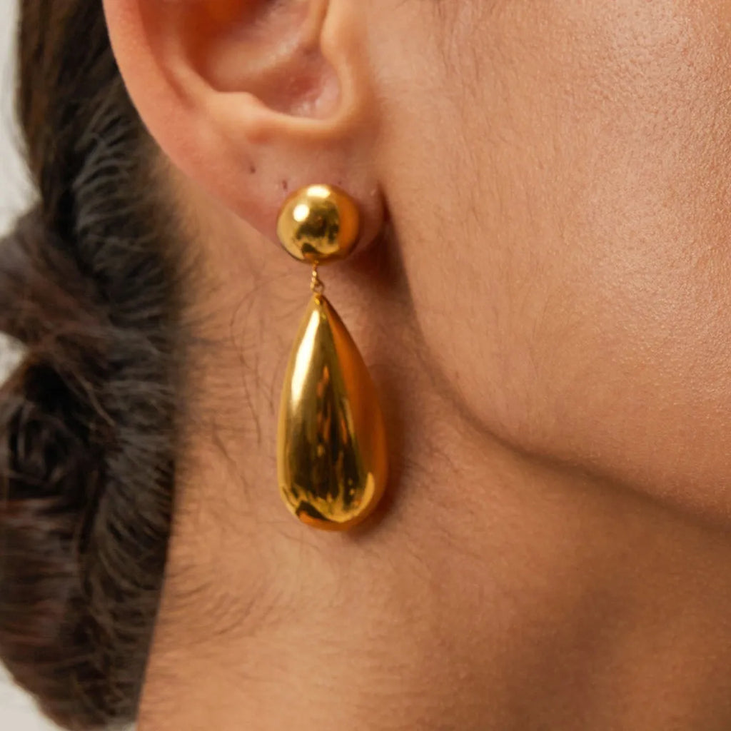 Gold-coloured stainless steel earrings featuring a geometric hemisphere shape with a dangling water drop pendant.