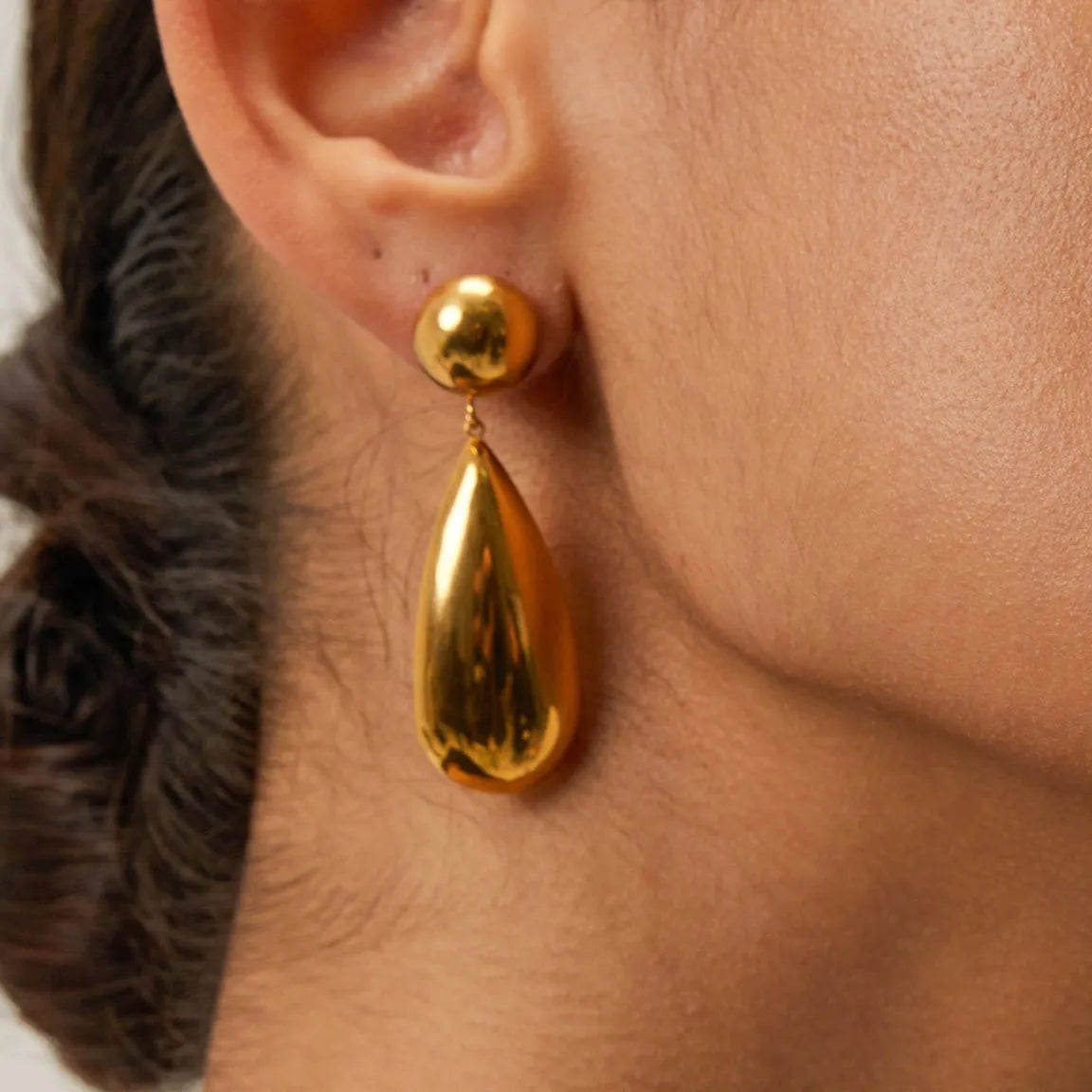 Gold-coloured stainless steel earrings featuring a geometric hemisphere shape with a dangling water drop pendant.