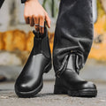Vintage brown Chelsea boots with frosted finish and car suture detailing on a wooden floor.