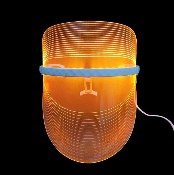 Transparent ABS LED light therapy face mask with red blue yellow lights and USB cable on a flat surface