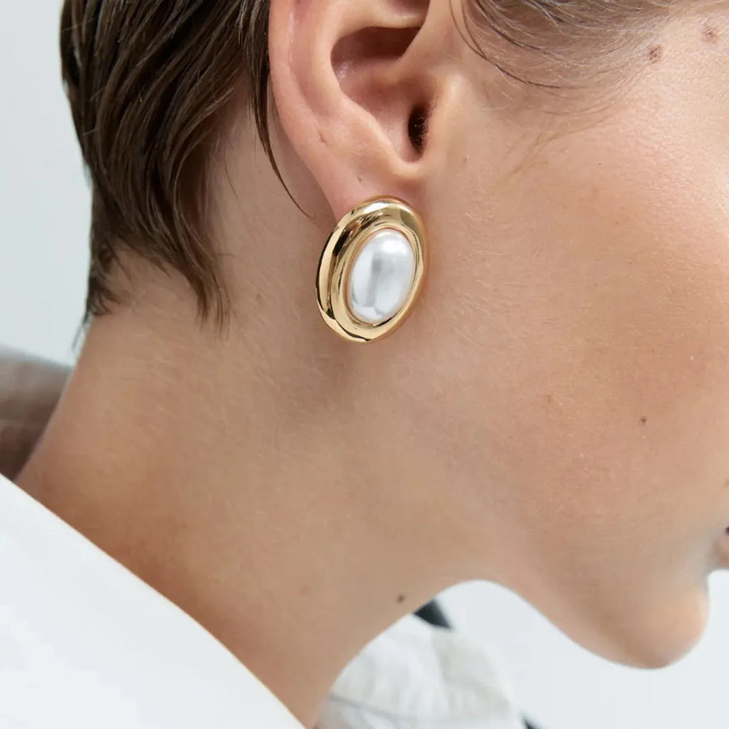 A pair of stainless steel post ear studs with small vintage-style pearl accents on a silver-tone background.
