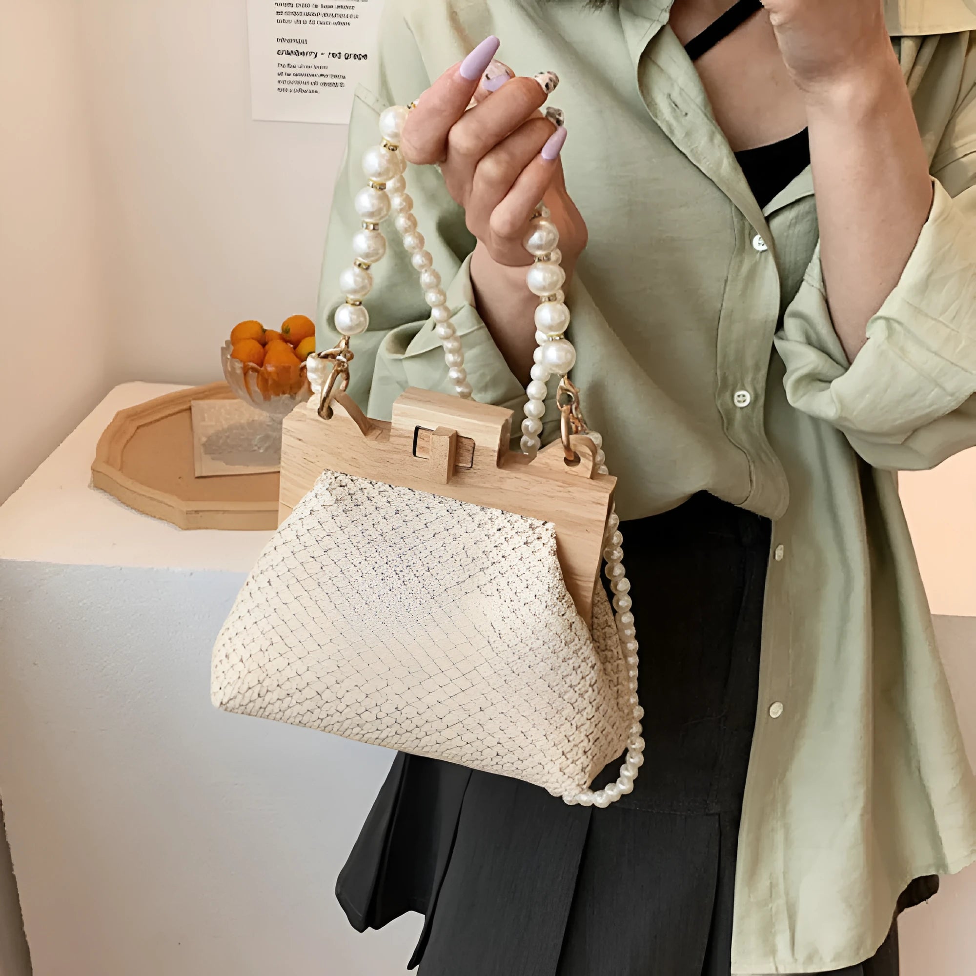 Women's woven straw shoulder bag with pearl chain strap in beige, showing its horizontal square shape.