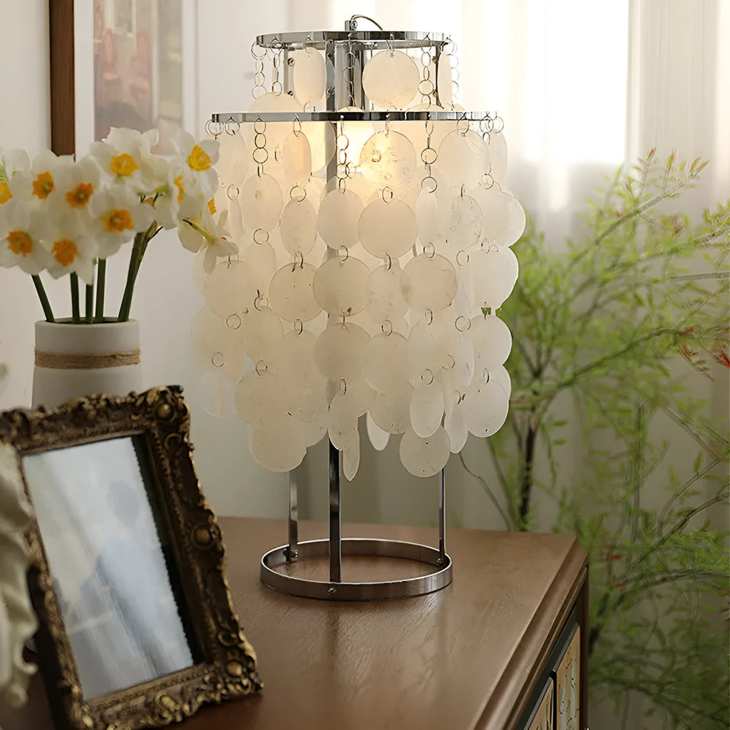 Modern shell-shaped bedside table lamp in chrome metal finish on a wooden surface.