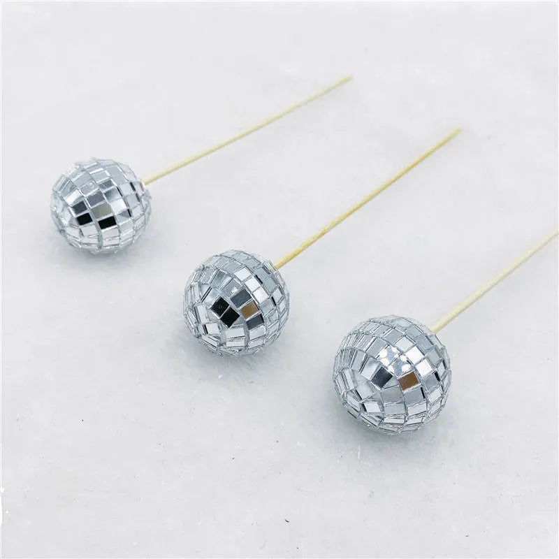 Glass disco ball cake decoration with a wooden stick inserted into a cake, showing reflective surface.