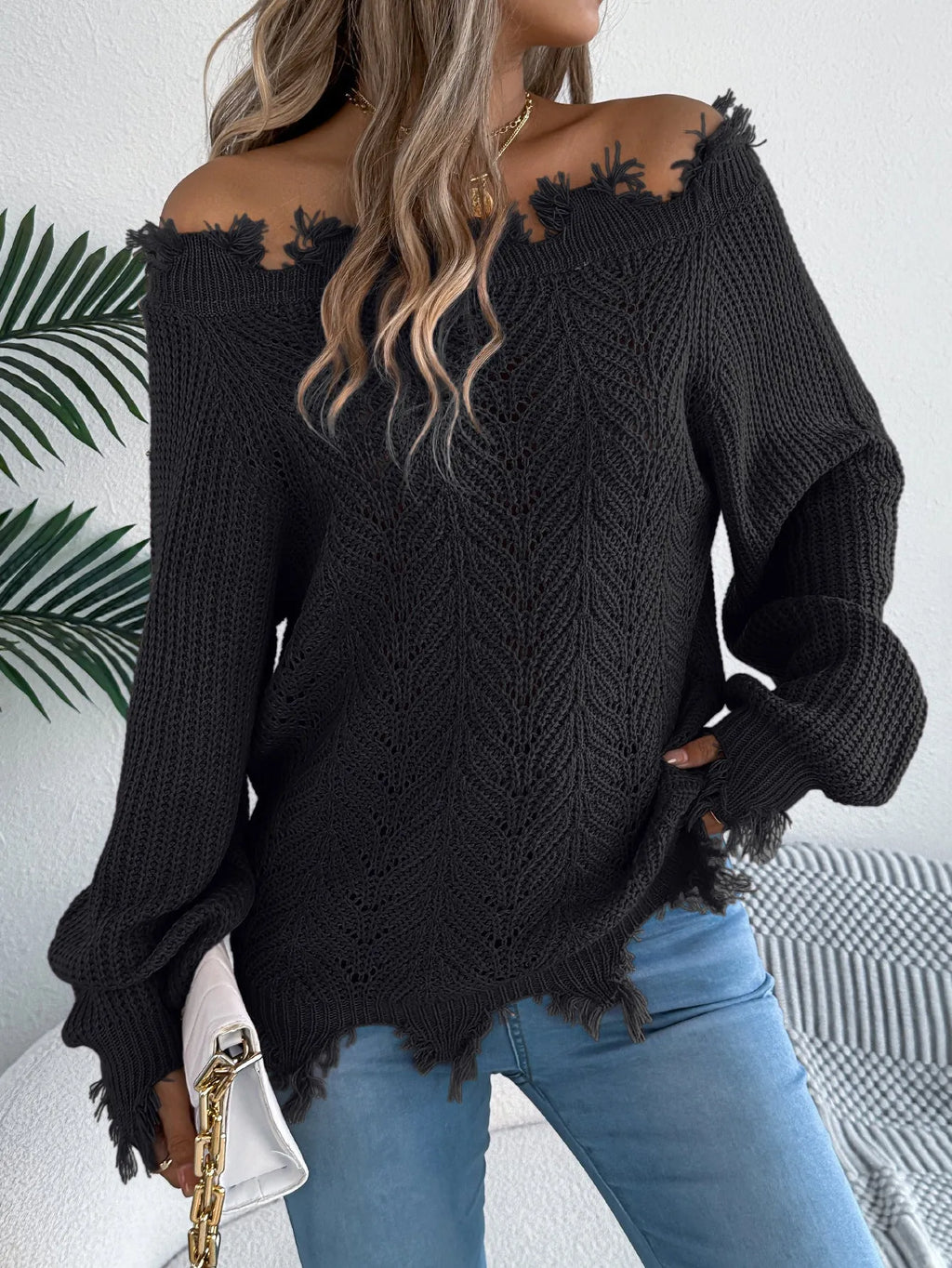 White hollow-out patterned long-sleeved sweater with a cut off-the-shoulder neckline on a model.