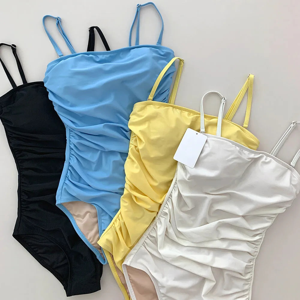 Women's sling style one-piece swimsuit with belly pleats in a solid colour.