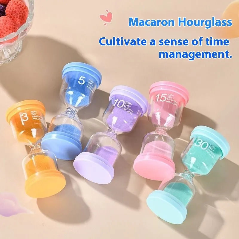 Handmade glass sand clock timer on a desk, showing purple sand flowing, with blue, green, and pink variants beside it.