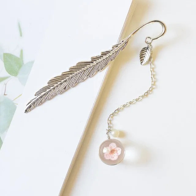 Dried flower sealed inside a rectangular silver metal bookmark with a hole at the top.