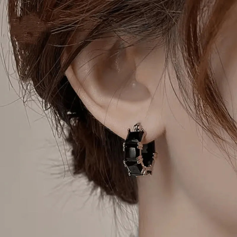 Geometric U-shaped gold earring with a round black zirconium stone on a copper base.