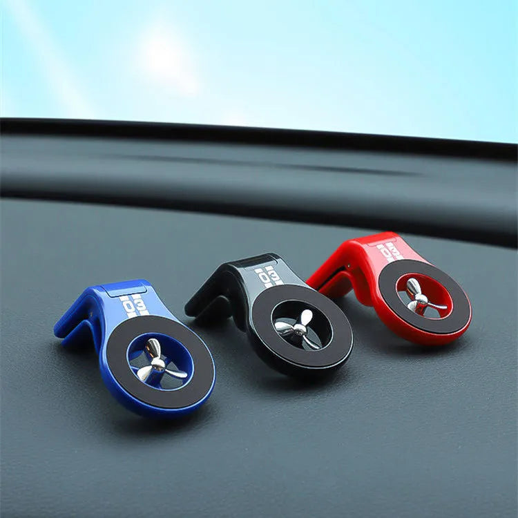 Black magnetic car phone holder clipped to a car air vent, holding a mobile phone, with a fragrant slice inserted.