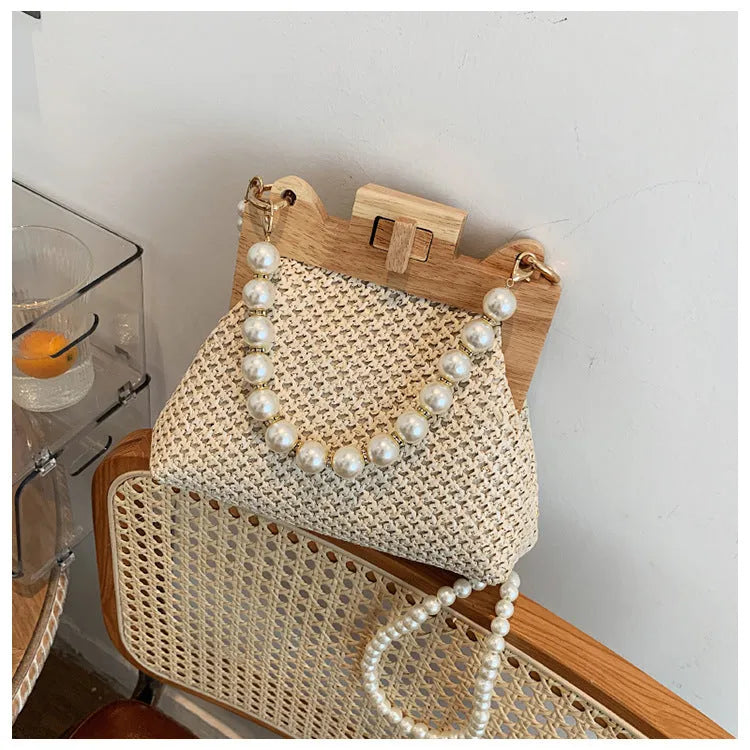 Women's woven straw shoulder bag with pearl chain strap in beige, showing its horizontal square shape.