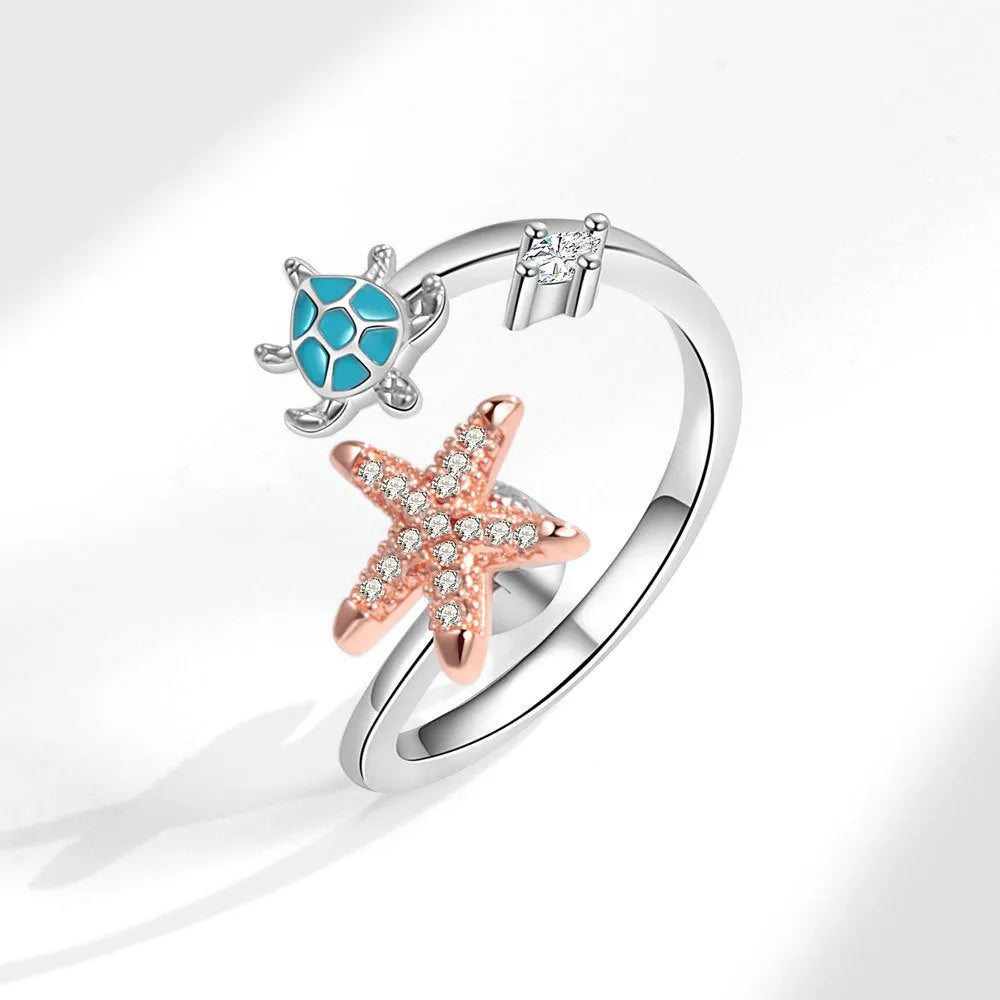 White gold copper spinning anxiety relief ring with turtle and starfish elements on a flat surface