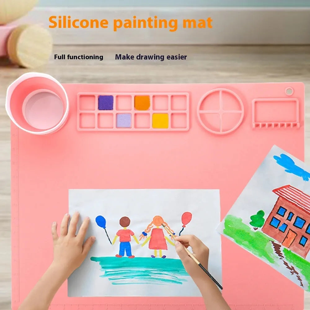 Light blue silicone painting mat with two recessed bowls for holding paint, placed on a wooden table.