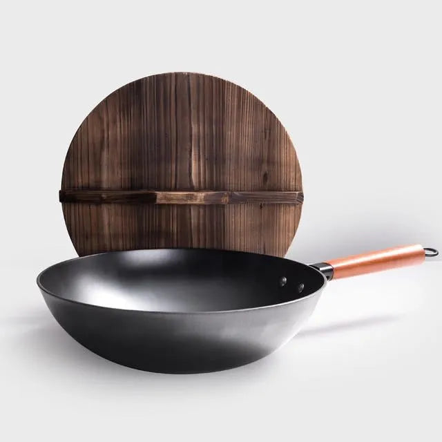 Black traditional handmade iron wok pan with a long wooden handle on a kitchen hob.