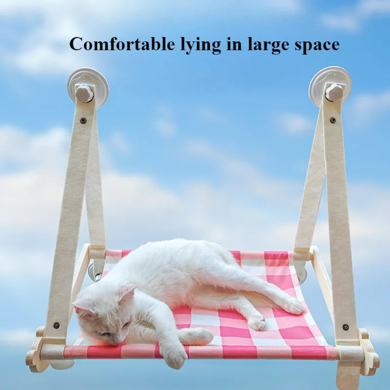 Pink wooden cat hammock bed with suction cups attached to a window, showing a cat lying on the linen mat.