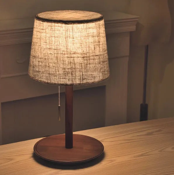 Walnut colour solid wood bedside lamp with a white fabric lampshade and a black cable switch.