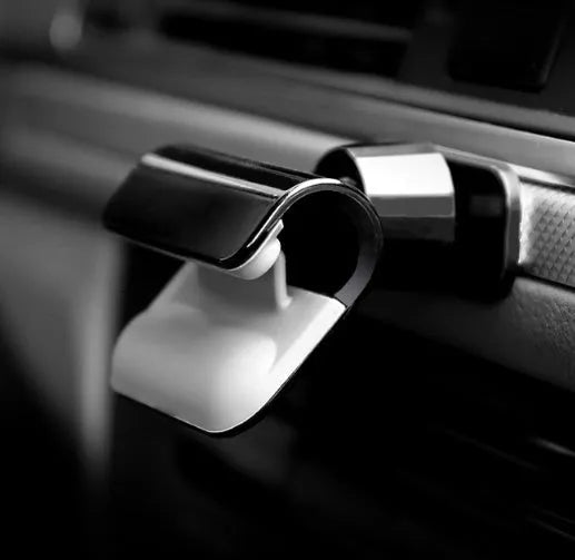 Black 360-degree rotating gravity car phone holder mounted on a car dashboard, holding a mobile phone.