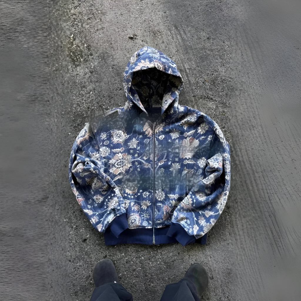 A man's loose fitting blue hooded zip-up coat with long sleeves on a hanger.
