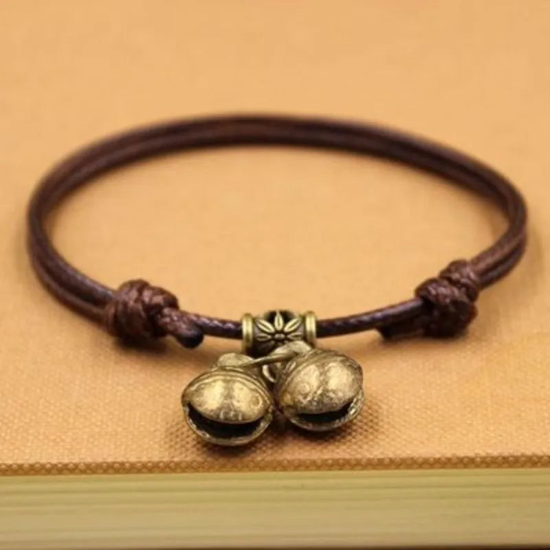 Black nylon rope dog collar with a brass bell on a wooden surface.