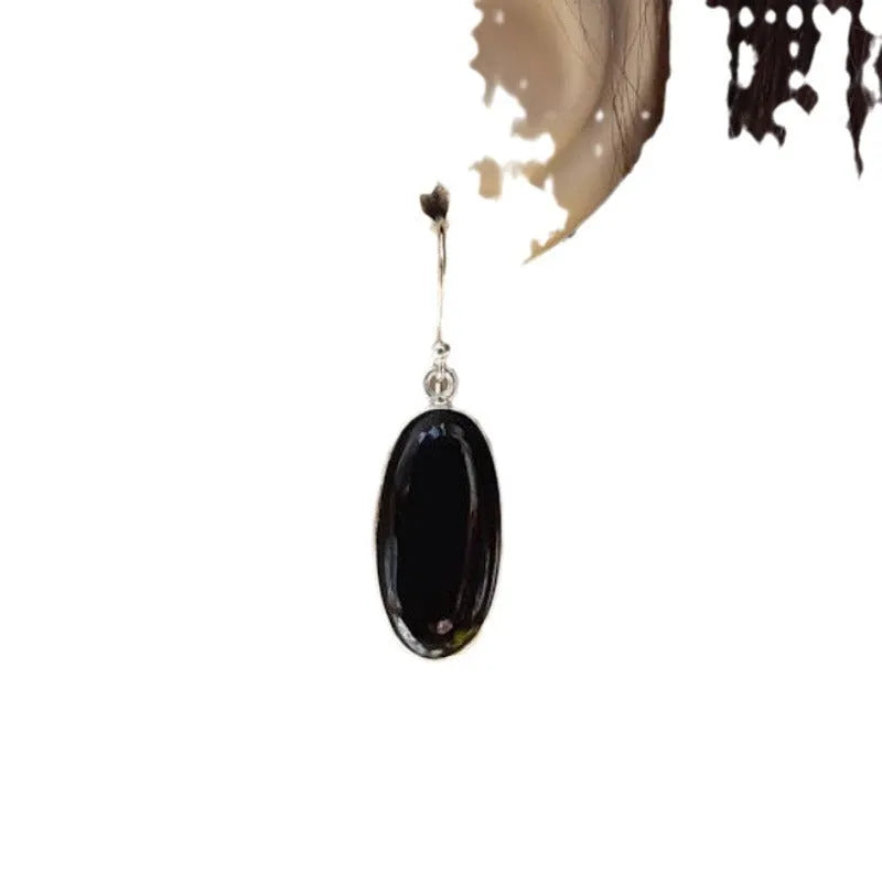 Close-up of women's earrings with black agate oval pendant and silver electroplated geometrical alloy design.