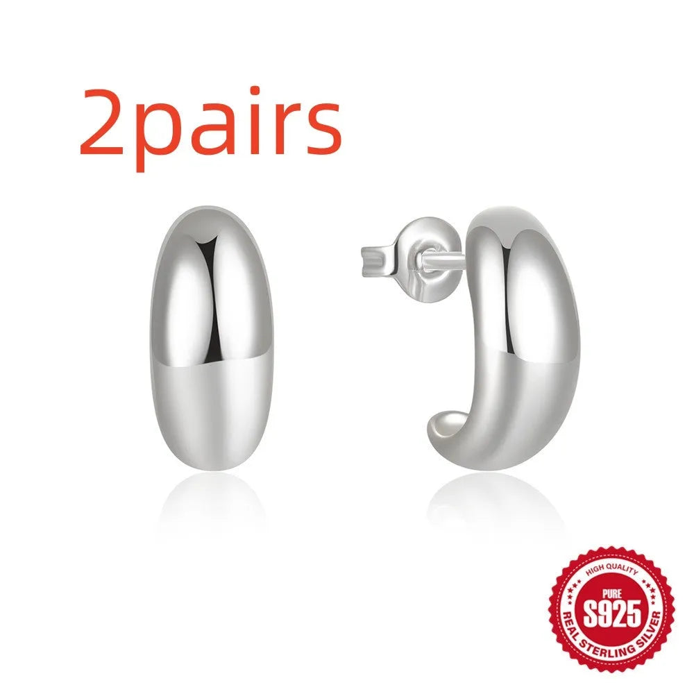 Close-up of a glossy C-shaped sterling silver stud earring with a gold electroplated finish.
