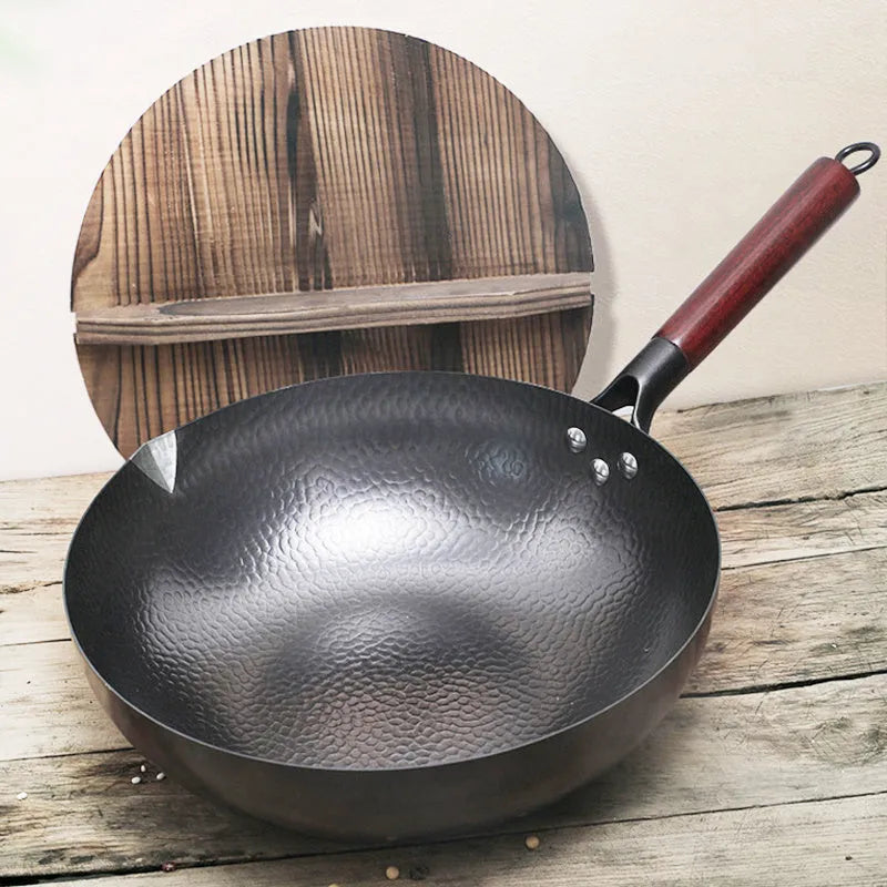 Black traditional handmade iron wok pan with a long wooden handle on a kitchen hob.