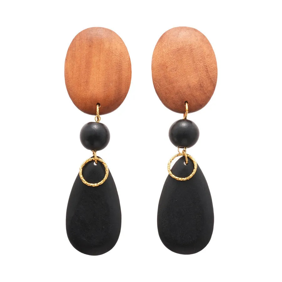 Close-up of handmade brown and black wooden ellipse earrings with silver needle fastenings on a textured background.