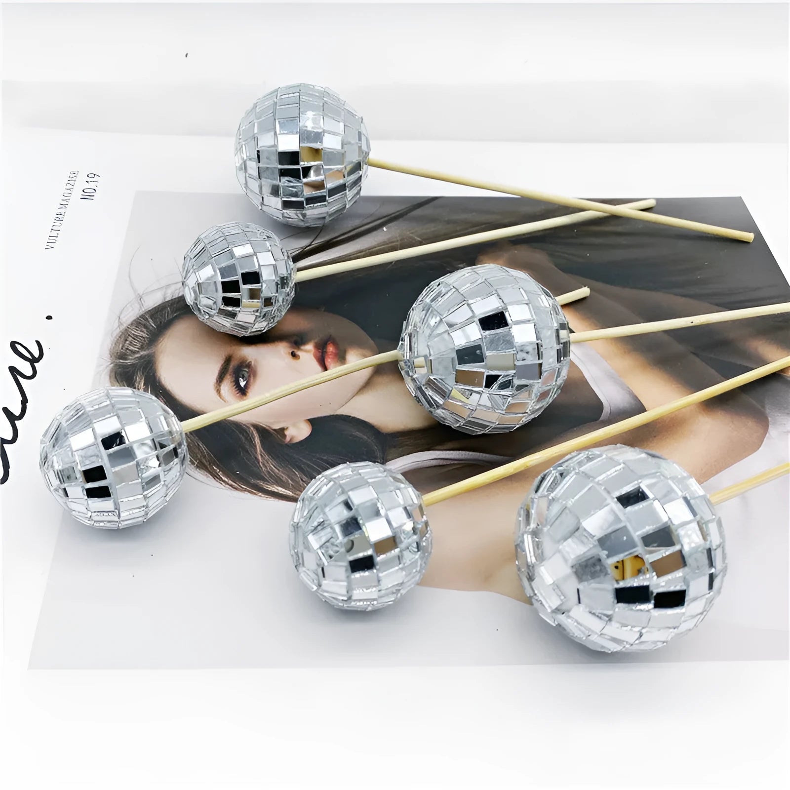 Glass disco ball cake decoration with a wooden stick inserted into a cake, showing reflective surface.